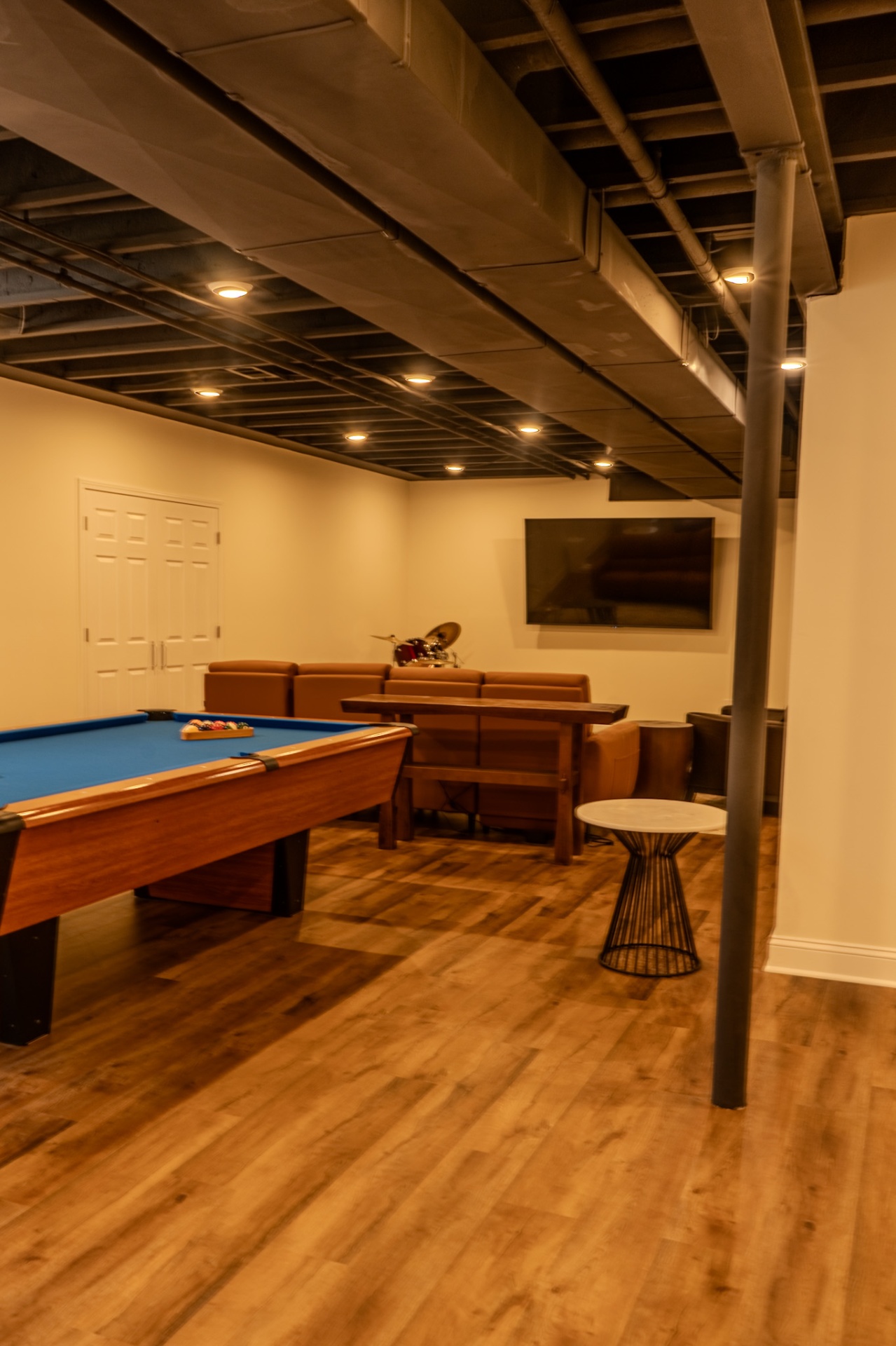 Real finished basement man cave with blue pool table, brown leather sectional, wall-mounted TV, and black exposed ceiling by Arch Basements.
