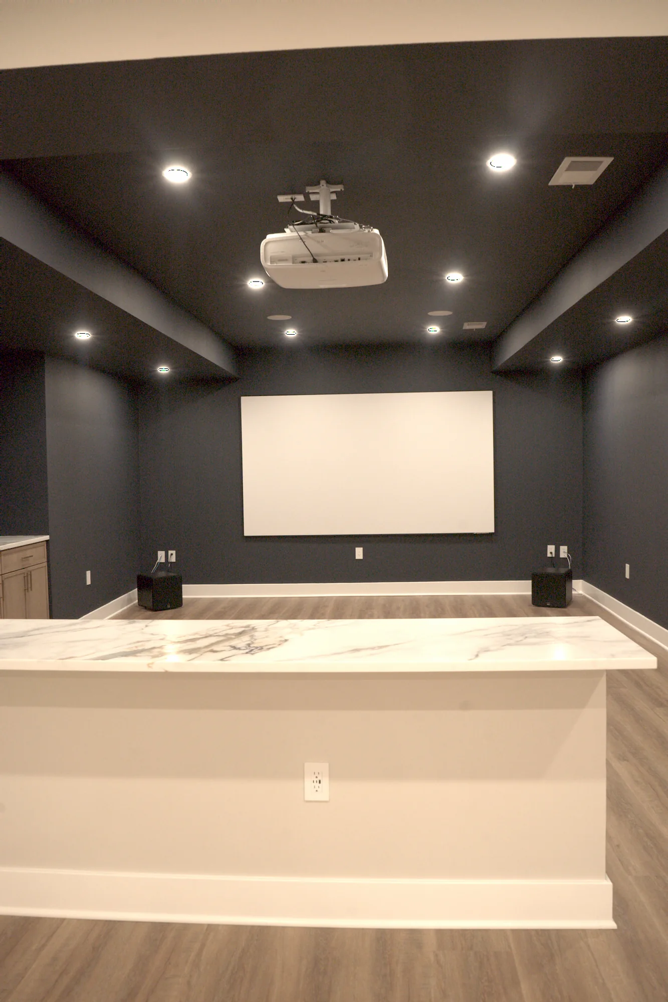 Finished basement home theater with projector screen and dark accent walls by Arch Basements.