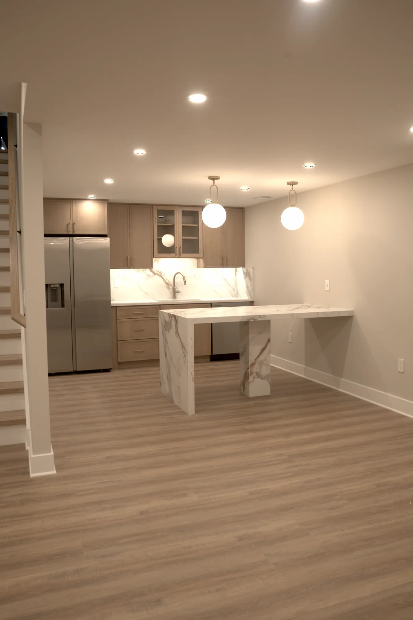 Finished basement wet bar with marble island, pendant lights, and cabinetry by Arch Basements.