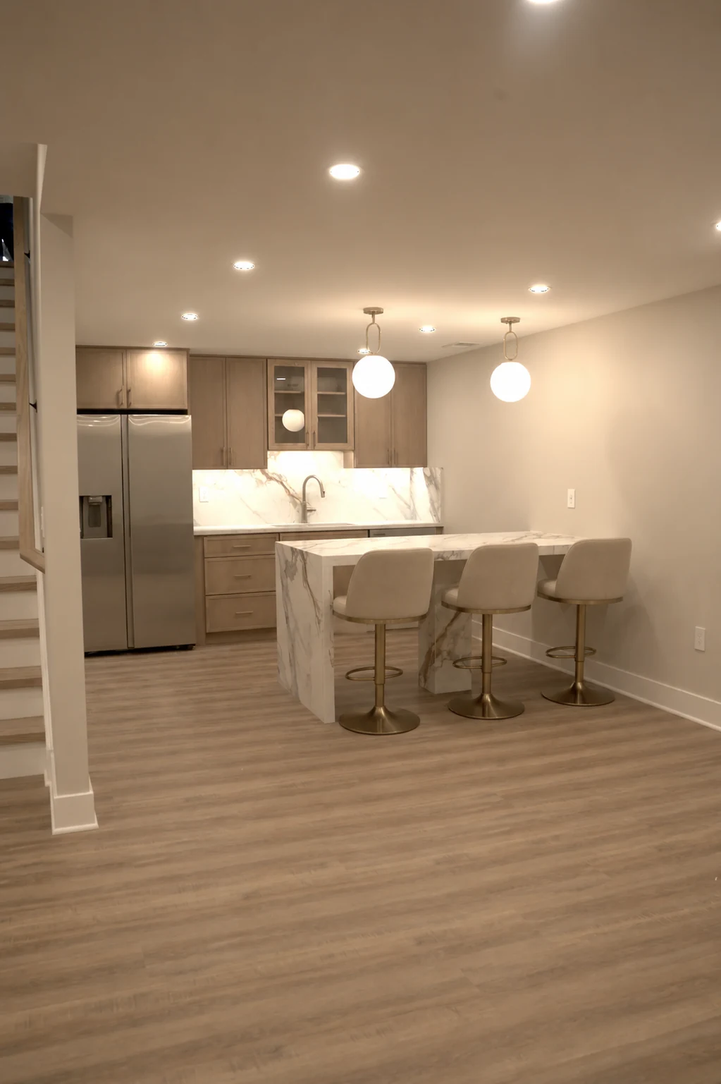 Modern finished basement kitchenette with marble island, pendant lighting, and upscale swivel bar stools by Arch GC.